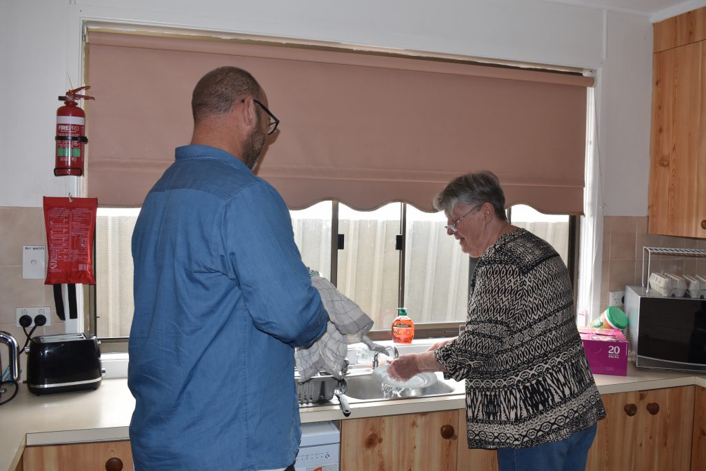 Man and woman standing in a kitchen, man helping woman with dishes