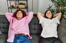 Mature mother and down syndrome daughter at home resting on the sofa