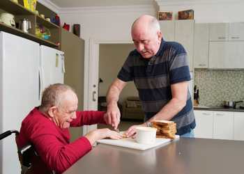 Home Career assisting Man with a Disability in a wheelchair making a sandwich in the kitchen